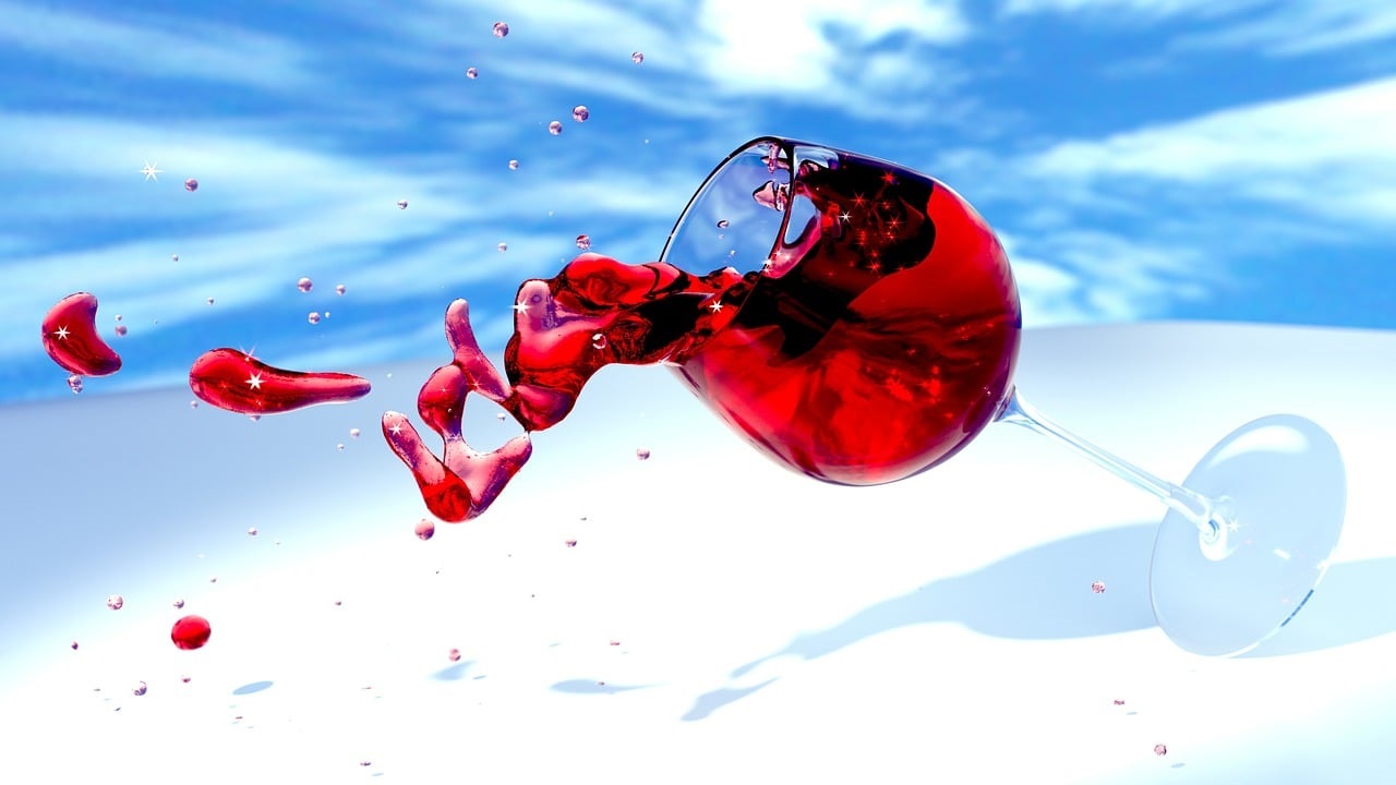 Dekoratives Bild Weinprobe | umkippendes Weinglas mit Rotwein, im Hintergrund blauer Himmel mit Wolken