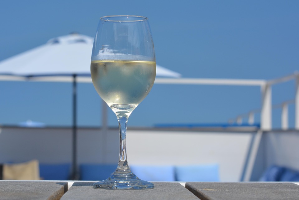 Dekoratives Bild Weintalk | Weißweinglas, im Hintergrund Sonnenschirm und blauer Himmel