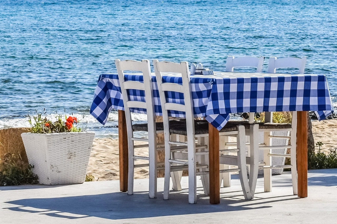 Dekoratives Bild Weinprobe | Terrasse mit Tisch und Stühlen, im Hintergrund das Meer